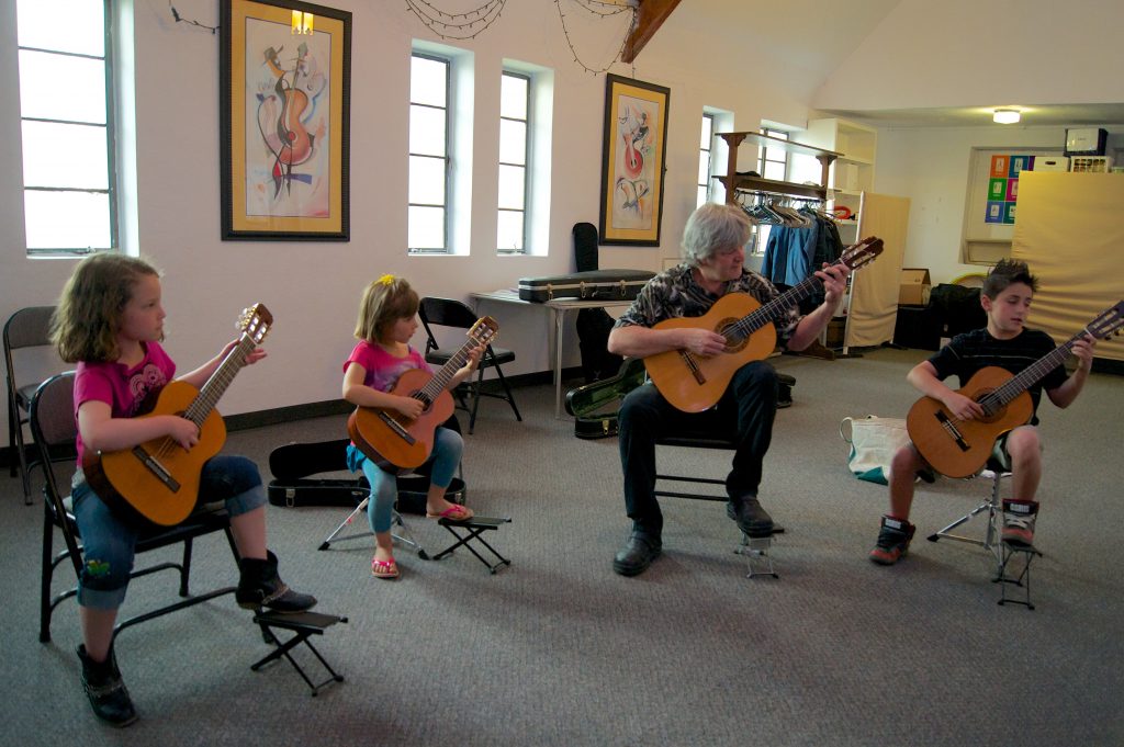 A group of children play guitars with an adult teacher at our Colorado community music school.
