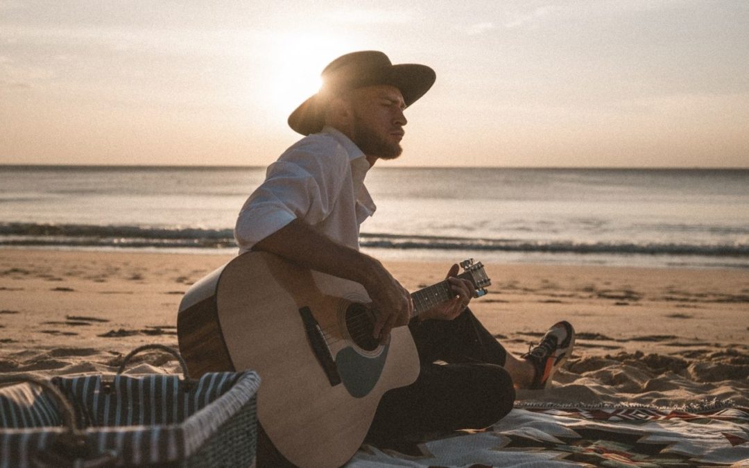 Person playing guitar on the beach in the summer - easy ways to play music over the summer